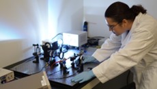 A woman in a lab coat (me) bent down over a optical test bench